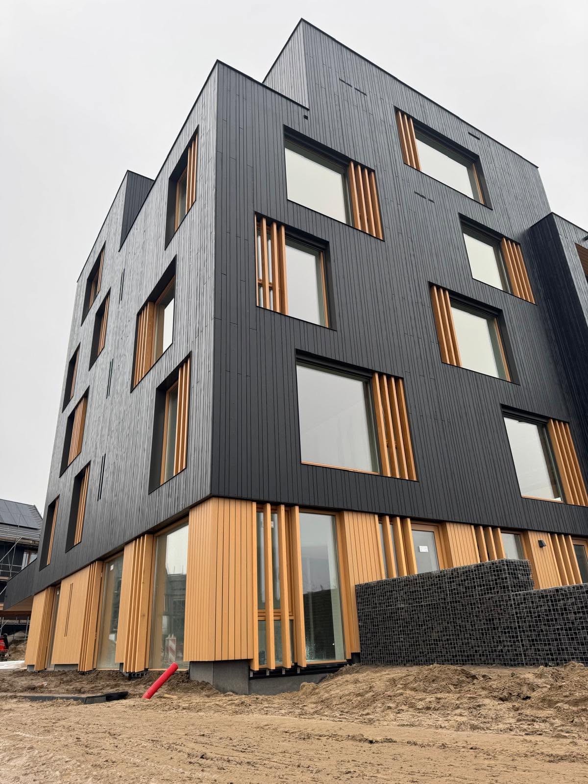 Appartementengebouw met zwarte vuren gevelbekleding en houten accenten bij project Stelt